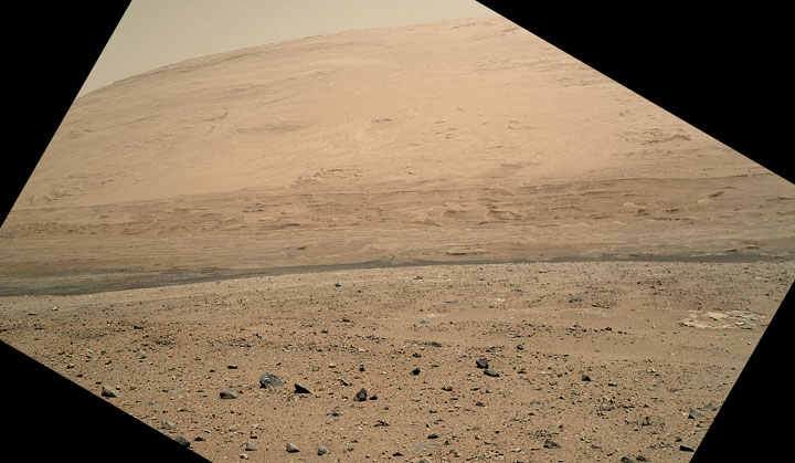 Curiosity as it crosses Gale Crater on Mars, looking toward Mount Sharp. The image is tilted because the camera, the Mars Hand Lens Imager, is carried at an angle when the arm is stowed for driving.
