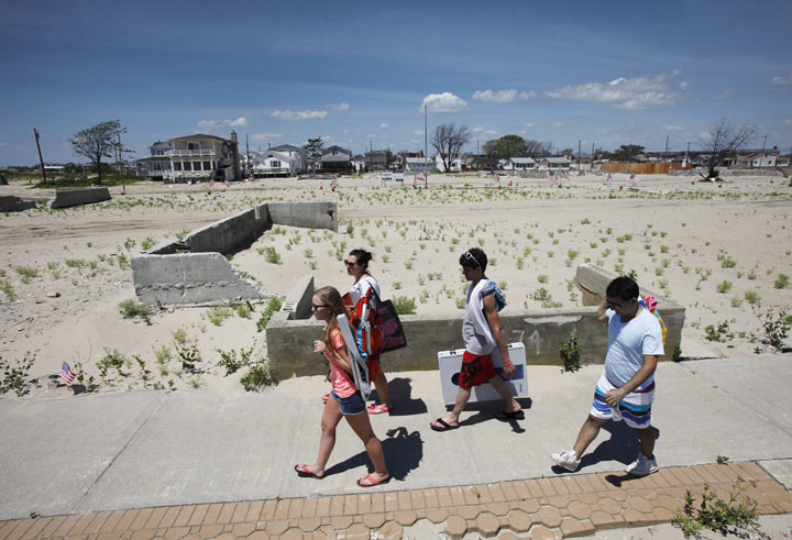 People walk to the beach in the Breezy Point section of the Queens borough of New York, Saturday, July 6, 2013, past the cleared site where 111 homes burned to the ground during Superstorm Sandy the night of Oct. 29, 2012. 