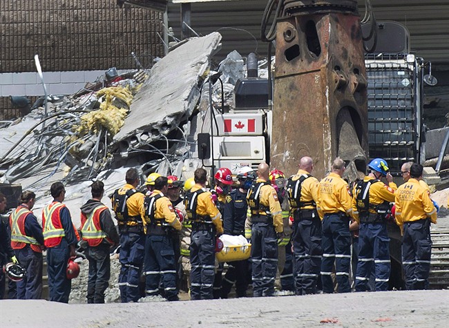 Rescue workers remove their hard hats as firefighters carry a second body out of the Algo Centre Mall in Elliot Lake, Ont., on June 27, 2012, after the mall's roof collapsed. 