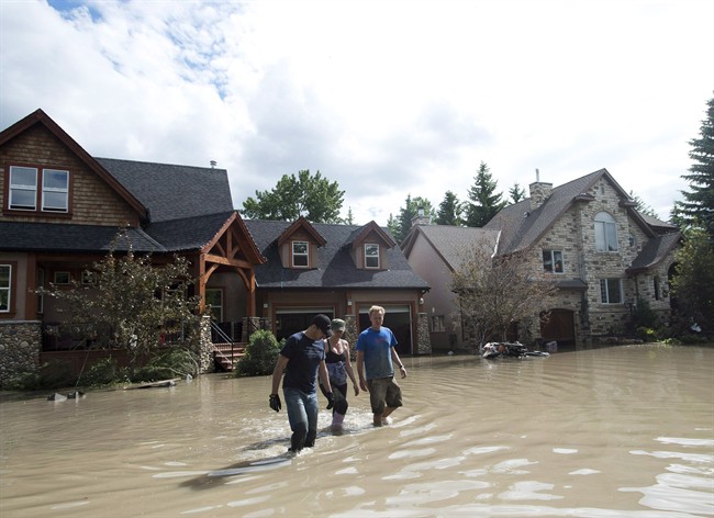 Residents walk through flood waters in Calgary on June 24, 2013. The Alberta government says homeowners and small businesses affected by last month's severe flooding can expect a rebuild, but they won't be entitled to hardwood floors or granite counter tops.