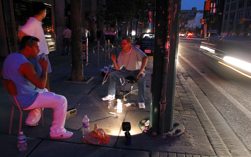 Chris Litras (r) sits outside his shop in downtown Toronto August 14, 2003 to keep an eye on things until the power comes back on during a blackout that affected parts of Canada and the North Eastern United States.