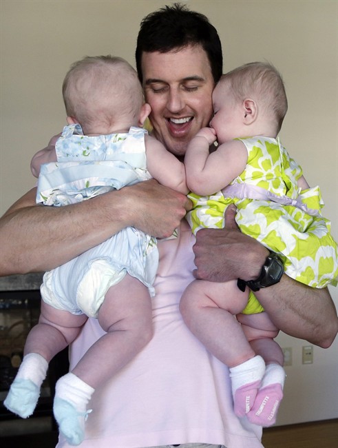 In this Tuesday, Aug. 20, 2013 photo, Trey Powell cuddles his six-month-old daughters Kylan, left, and Ashton in their home in Seattle. 