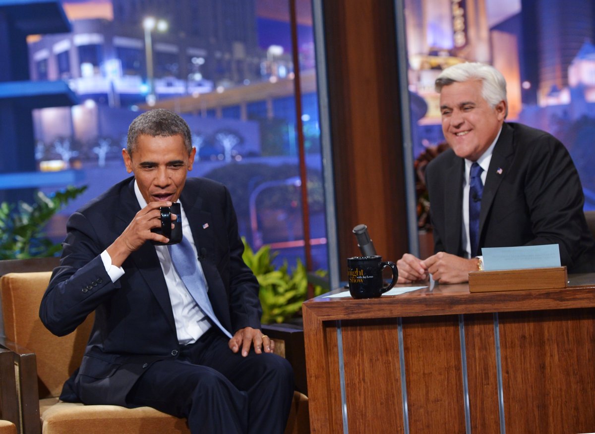 US President Barack Obama takes a drink from a mug as host Jay Leno watches during a taping of The Tonight Show with Jay Leno at NBC Studios on August 6, 2013 in Burbank, California.