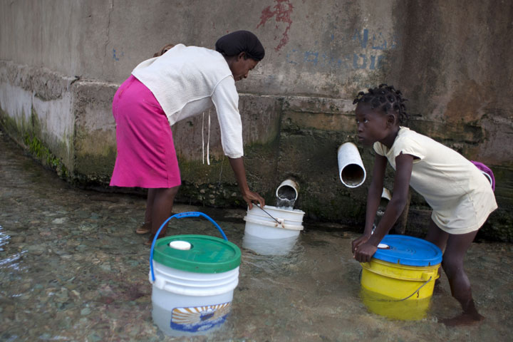 In this Aug. 22, 2013 photo, a girl pushes down the lid on her her bucket filled with water she collected from the pipe that captures mountain water in Thomazeau, Haiti. 
