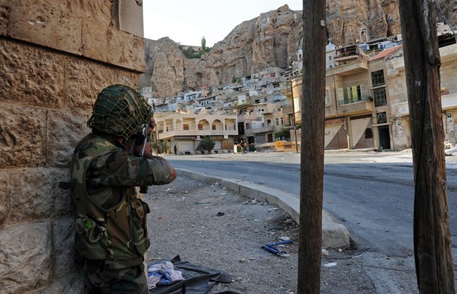 In this Wednesday, Sept. 11, 2013 photo released by the Syrian official news agency SANA, a Syrian government solider aims his weapon during clashes with Free Syrian Army fighters, not pictured, in Maaloula village, northeast of the capital Damascus, Syria. 