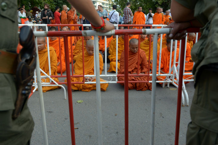 Cambodian police officials stand guard as Buddhist monks meditate for peace near the Royal Palace in Phnom Penh on September 19, 2013 as protesters requested Cambodia's King Norodom Sihamoni to delay the first parliament meeting scheduled on September 23. Cambodia's king appealed to opposition lawmakers on September 18, to drop a planned boycott of parliament for the sake of 'national unity' following strongman premier Hun Sen's disputed election win. 