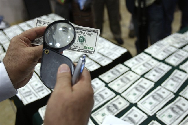 FILE - In this Aug. 17, 2012 file photo, a police officer inspects an alleged counterfeit $100 U.S. dollar note during a media presentation in Lima, Peru.