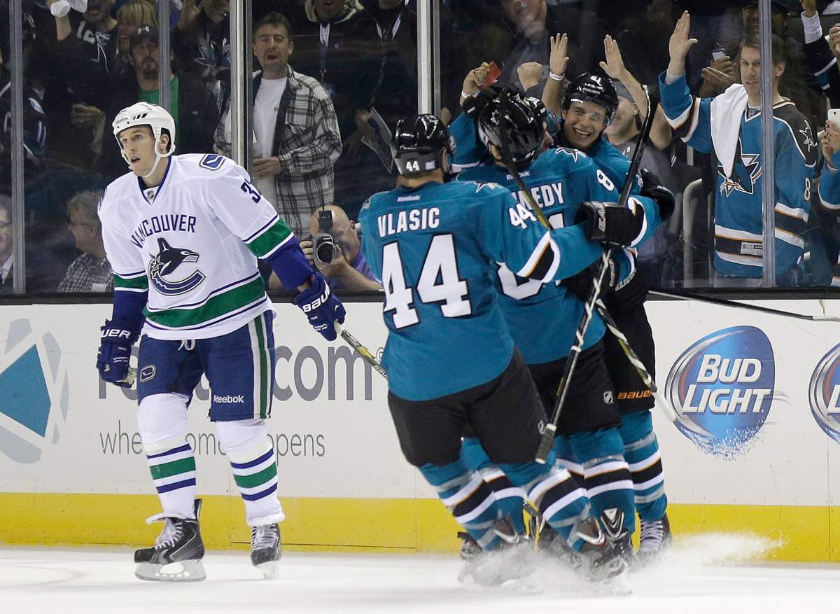 San Jose Sharks' Justin Braun, right, is hugged by teammates Tyler Kennedy and Marc-Edouard Vlasic (44) after scoring against the Vancouver Canucks during the second period of an NHL hockey game on Thursday, Oct. 3, 2013, in San Jose, Calif. Canucks' Dale Weise is at left. (AP Photo/Marcio Jose Sanchez).