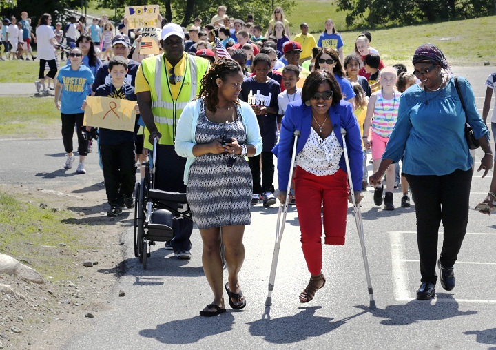 In this Wednesday, June 5, 2013 photo, Mery Daniel, a Boston Marathon bombing survivor, uses borrowed crutches as she walks with students during a fundraising walkathon for her, at the William Seach Primary School in Weymouth, Mass. Students at the school raised more than $8,000 for Daniel, whose father Hary Volmar, pushing wheelchair, is one of their bus drivers. Flanking Daniel is her mother-in-law, Marie Daniel, right, and cousin Yvrantz Celestin, left. (AP Photo/Charles Krupa)