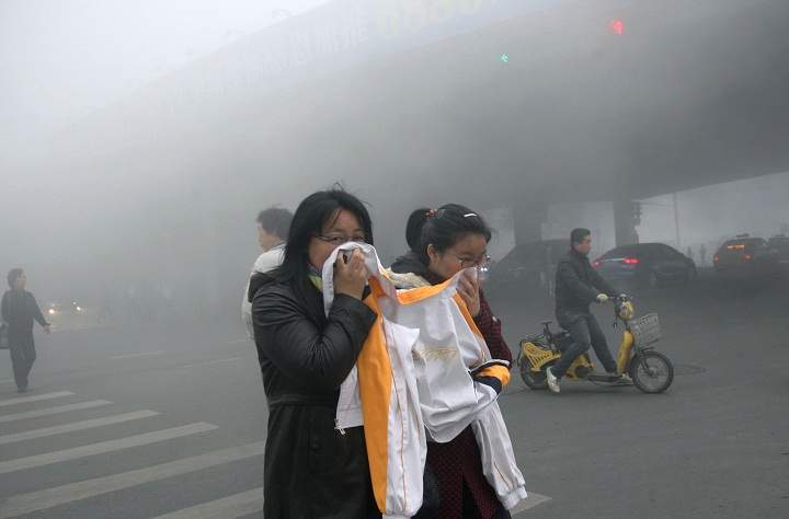 Two women cover up their mouths and noses with a jacket as they cross a street covered by dense smog in Harbin, northern China, Monday, Oct. 21, 2013. Visibility shrank to less than half a football field and small-particle pollution soared to a record 40 times higher than an international safety standard in one northern Chinese city as the region entered its high-smog season. (AP Photo/Kyodo News)