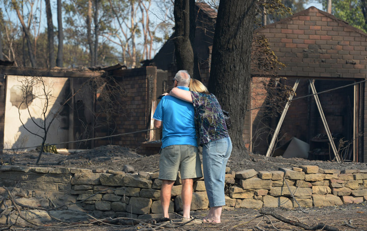 A couple look at a house burnt out by bushfires in Winmalee in Sydney’s Blue Mountains on October 18, 2013. (Photo credit: Getty Images)