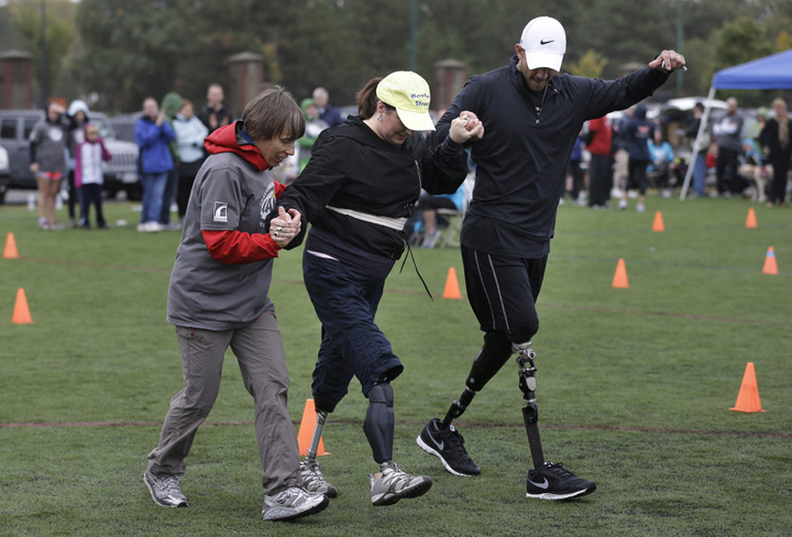 Celeste Corcoran, center, of Lowell, Mass., who lost her legs in the 2013 Boston Marathon explosion, is assisted by Ann-Marie Starck, of Ashford, Conn., left, and Gabriel Martinez, of Golden, Colo., right, during a running clinic for challenged athletes Sunday, Oct. 6, 2013, in Cambridge, Mass.