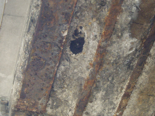 Photo of a hole in the bottom of the Dufferin Bridge from Webb’s Feb. 2008 report. The bottom of the asphalt surface is visible through a hole in the concrete.