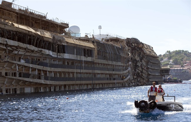In this Sept. 18, 2013 file photo, a small boat navigates past the damaged side of the Costa Concordia ship after it was pulled upright, on the Tuscan Island of Giglio, Italy.