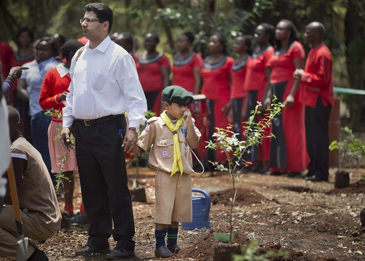 Khalil Rashid, 6, wears a scouts uniform as he holds the hand of his father and waits to plant a tree in memory of his schoolmate Jennah Bawa, 8, from Britain, who was shot along with her mother Zahira, at a memorial service and tree-planting marking the one-month anniversary of the the Sept. 21 Westgate Mall terrorist attack, in Karura Forest in Nairobi, Kenya Monday, Oct. 21, 2013. Families and friends of those killed in the attack planted trees in memory of lost loved ones in a ceremony that stressed that the attack occurred against people of all races and religions.