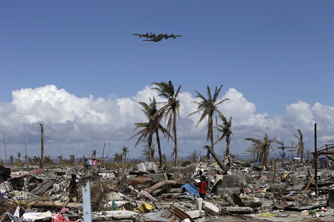 A US Navy C-130 cargo plane carrying typhoon survivors, flies over the devastation, as others sift through the debris in Tacloban city Monday Nov. 25, 2013 in Leyte province in central Philippines. THE CANADIAN PRESS/AP, Bullit Marquez.