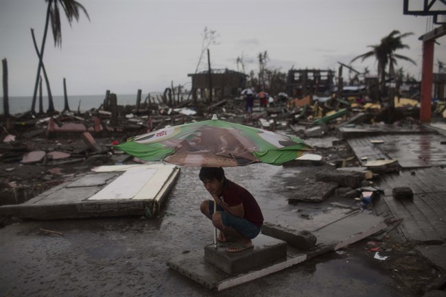 A Typhoon Haiyan survivor uses a market umbrella to protect himself from the rain in his destroyed neighborhood in Tacloban, Philippines on Friday Nov. 22, 2013. (Photo credit: AP Photo)