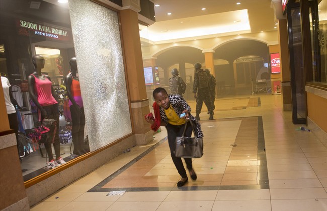 In this Saturday, Sept. 21, 2013 file photo, a woman who had been hiding during the gun battle runs for cover after armed police enter the Westgate Mall in Nairobi, Kenya, after gunmen threw grenades and opened fire.