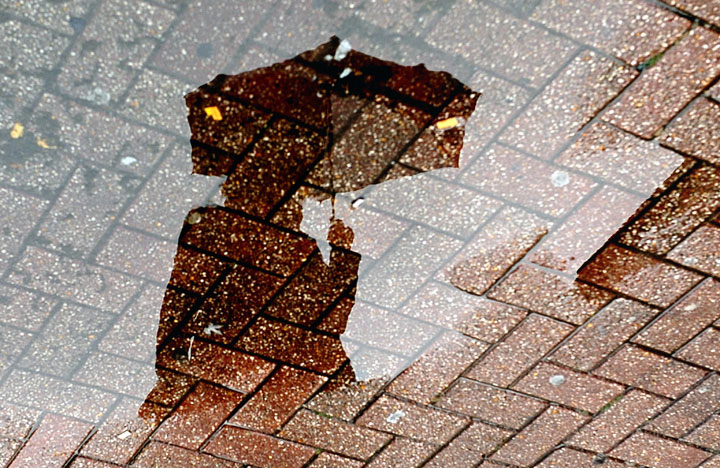 FILE: A reflection in a puddle of someone standing with an umbrella.