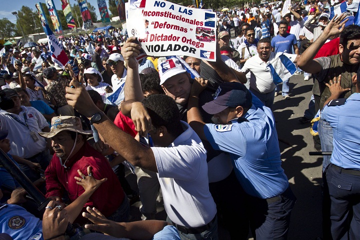 Opponents of Nicaraguan President Daniel Ortega clash with police during a protest against proposed constitutional reforms, in front of the National Assembly in Managua, Nicaragua, Thursday, Nov. 28, 2013. The proposed reforms include removing presidential term limits and allowing military and police personnel to run for government office. The banner at the top of the frame, playing off the words constitutional reforms, reads in Spanish; "No to the 'unconstitutional deforms" of the dictator Ortega. Rapist." In 1998 Ortega's step-daughter Zoilamerica accused the Sandinista leader of sexual abuse.