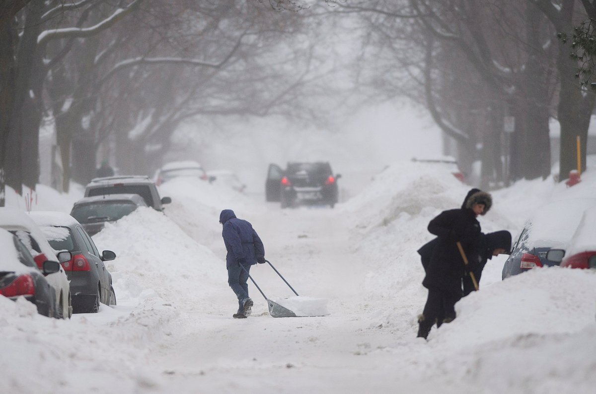 People clear snow from around their cars on a street in Montreal.