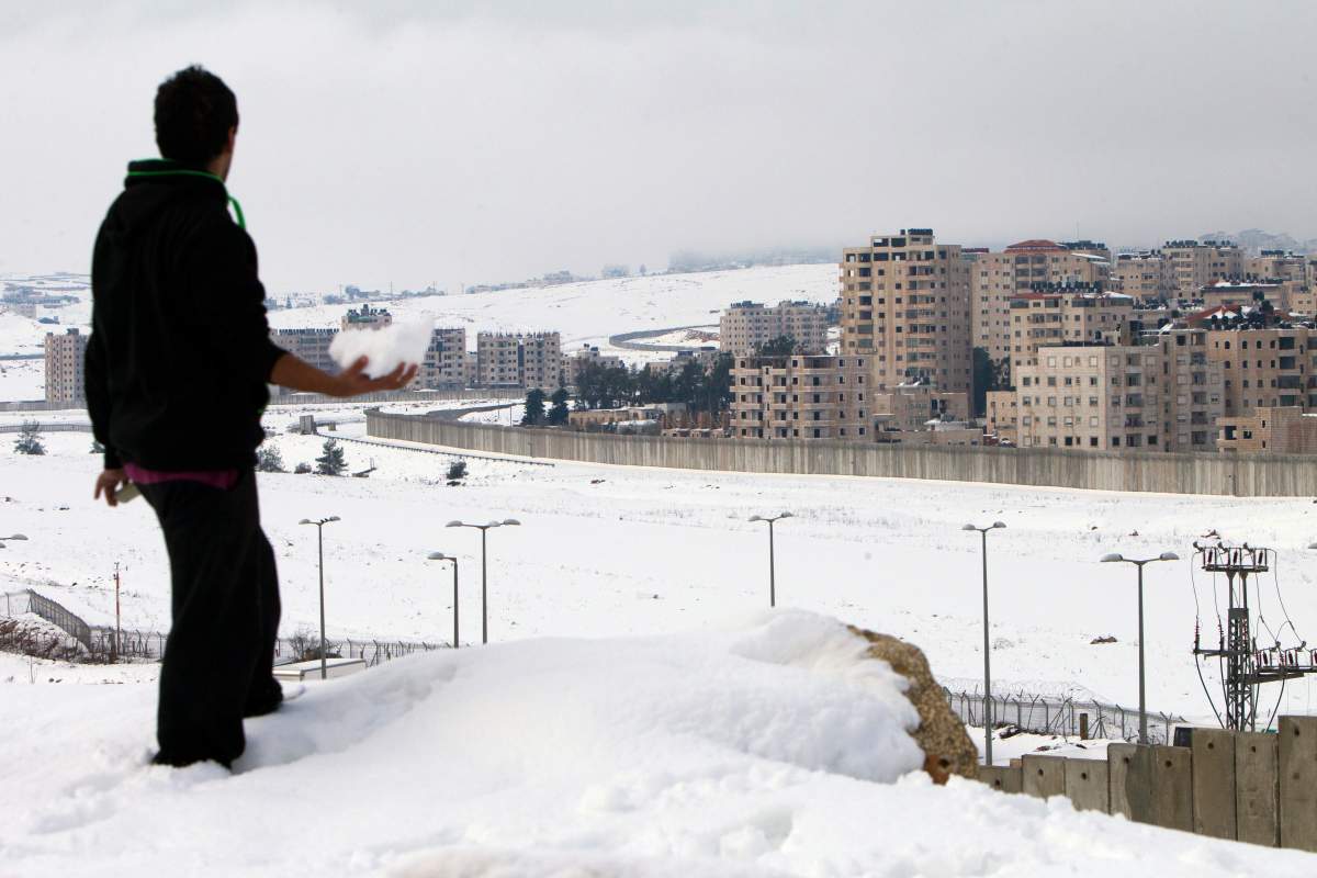 A Palestinian man carries snow next to a section of Israel's controversial separation barrier in the West Bank village of Al-Ram on the outskirts of Jerusalem on December 14, 2013, following a snowstorm. AFP PHOTO/AHMAD GHARABLI (Photo credit should read AHMAD GHARABLI/AFP/Getty Images)