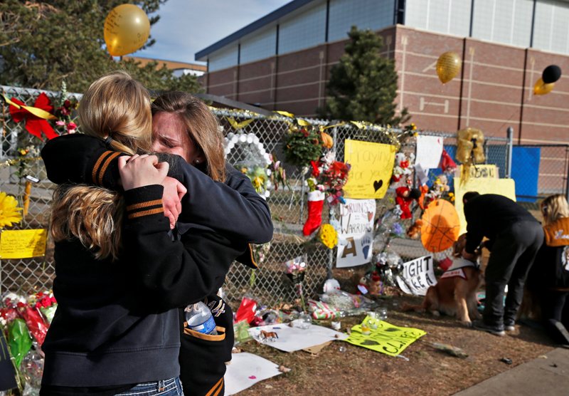 Arapahoe High School senior Lily Boettcher, right, and 2013 Arapahoe grad Joy Dafoe hug at a tribute site for severely wounded student Claire Davis, who was shot by a classmate during a school attack six days earlier at Arapahoe High School, in Centennial, Colo., Thursday Dec. 19, 2013. On Thursday, students were allowed back into school to retrieve their belongings. (AP Photo/Brennan Linsley).