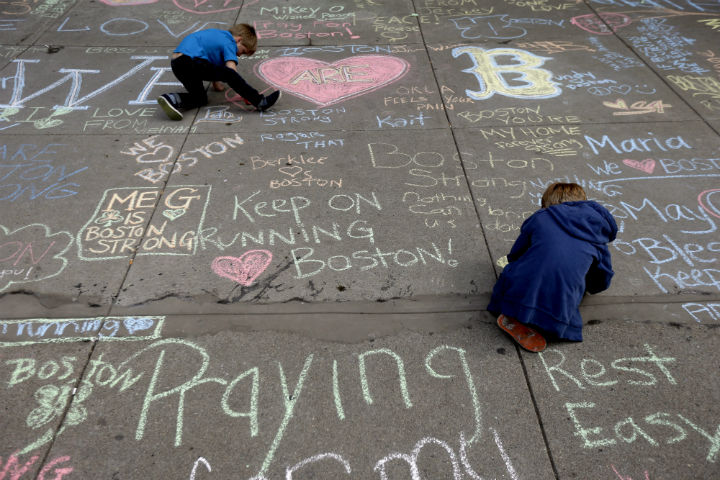 Two young boys leave messages with chalk on a sidewalk near the finish line of the Boston Marathon