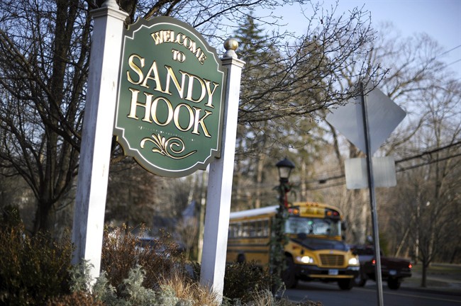 In this Dec. 4, 2013 file photo, a school bus drives past a lamppost decorated for the holidays, and a sign reading Welcome to Sandy Hook, in Newtown, Conn. 