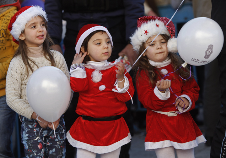 Palestinian children dressed up as Santa Claus pose for a photograph at Manger Square, outside the Church of the Nativity, traditionally believed by Christians to be the birthplace of Jesus Christ, in the West Bank town of Bethlehem, Tuesday, Dec. 24, 2013.
