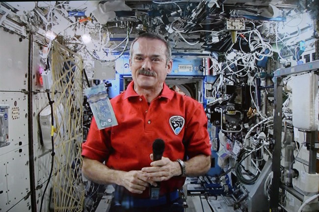 Astronaut Chris Hadfield poses for a photo with a new polymer $5 bank note on the International Space Station as seen via video link in Ottawa on April 30, 2013.