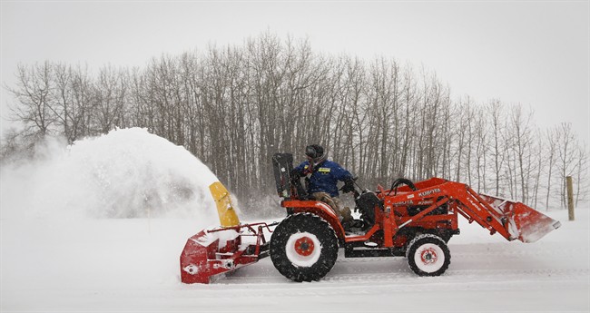 David Reid uses a snow blower mounted on a tractor to clear his driveway during a blizzard near Cremona, Alta., Monday, Dec. 2, 2013. 
