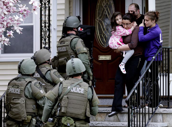 A woman carries a girl from their home as a SWAT team searching for a suspect in the Boston Marathon bombings enters the building in Watertown, Mass. (AP Photo/Charles Krupa, File)
.
