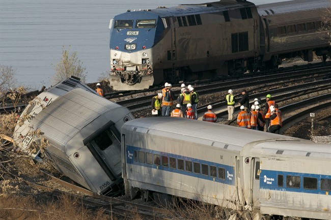 An Amtrak train, top, traveling on an unaffected track, passes a derailed Metro North commuter train, Sunday, Dec. 1, 2013 in the Bronx borough of New York. Officials are standing on a curve in the tracks where the Metro North train derailed. (AP Photo/Mark Lennihan)