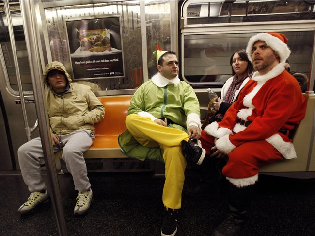 FILE - In this Dec. 11, 2010 file photo, John Paul, center, of Manhattan, dressed as an Elf and Michael Smallwood, of Brooklyn, dressed as Santa ride the E train downtown in New York for the annual SantaCon pub crawl where participants dress up in Santa and other Christmas themed outfits. 