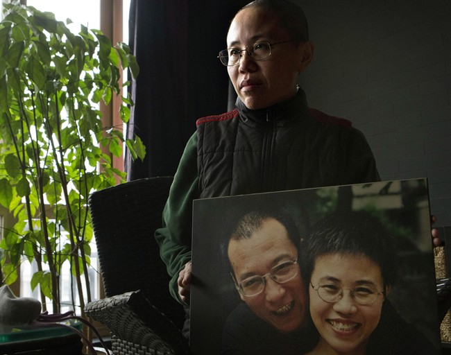 FILE - In this Dec. 6, 2012 file photo, Liu Xia, the wife of China's jailed Nobel Peace Prize laureate Liu Xiaobo, poses with a photo of her and her husband during an interview at her home in Beijing. (AP Photo/Ng Han Guan, File).