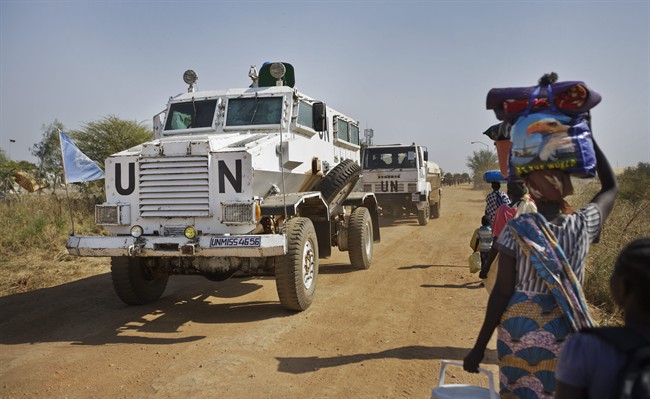 A United Nations armored vehicle travelling in convoy with a truck passes displaced people in violence-torn South Sudan in Dec. 2013.