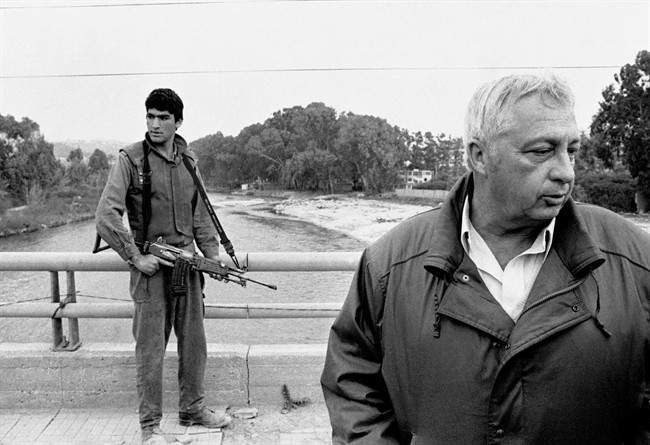 In this March 7, 1984 file photo, an Israeli soldier keeps his finger on the trigger of his assault rifle while Former Defense Minister Ariel Sharon, right, stands on the bridge overlooking the Awali River, Israel's most northerly position in Sidon, Lebanon.