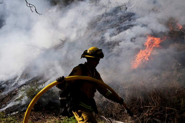 Firefighter Jeff Newby carries a water hose as he battles the Colby Fire on Friday, Jan. 17, 2014, near Azusa, Calif. 