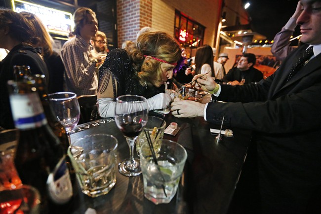 A server, right, behind an outdoor bar prepares marijuana for partygoers to smoke during a Prohibition-era themed New Year's Eve party celebrating the start of retail pot sales, at a bar in Denver, late Tuesday Dec. 31, 2013. 
