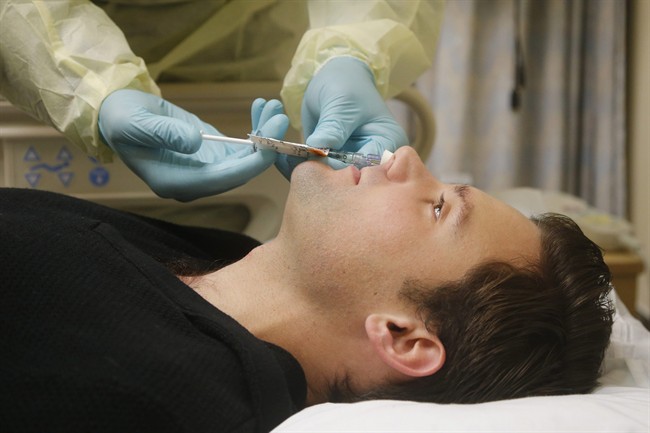 In this Jan. 14, 2014, photo, Daniel Bennett, 26, of College Park, Md., has live flu virus sprayed into his nose as part of a study at the National Institutes of Health in Bethesda, Md.