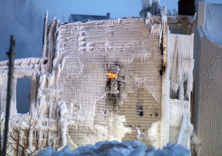 Flames flare up through a wall at the scene of a fatal fire which destroyed a seniors residence in L'Isle-Verte, Que., Thursday, January 23, 2014.