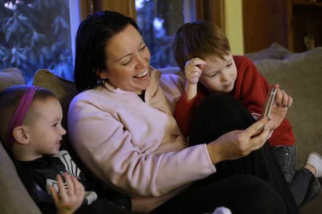 Julie Young, a Boston-based behavioral analyst, center, sits with her sons Nolan, 3, left, and Jameson, 4, right, while looking at a smart phone at their home, in Boston, Monday, Jan. 27, 2014.