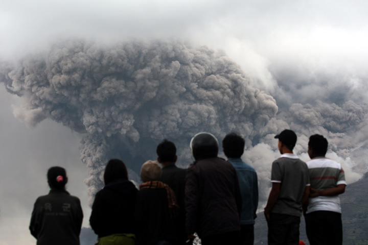 Villagers watch as Mount Sinabung releases pyroclastic flow during an eruption in Tiga Kicat, North Sumatra, Indonesia, Saturday, Jan. 4, 2014. 
