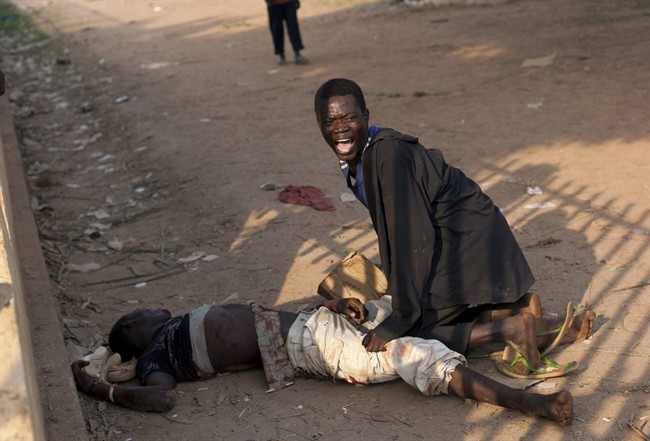 FILE - In this Monday, Dec. 23, 2013 file photo, a young man reacts after his friend was badly injured by passing Chadian troops in Bangui, Central African Republic. 
