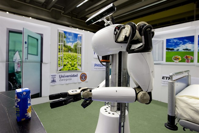 Amigo, a white robot the size of a person, uses information gathered by other robots to move towards a table to pick up a carton of milk and deliver it to an imaginary patient in a mock hospital room at the Technical University of Eindhoven, Netherlands, Wednesday Jan. 15, 2014.