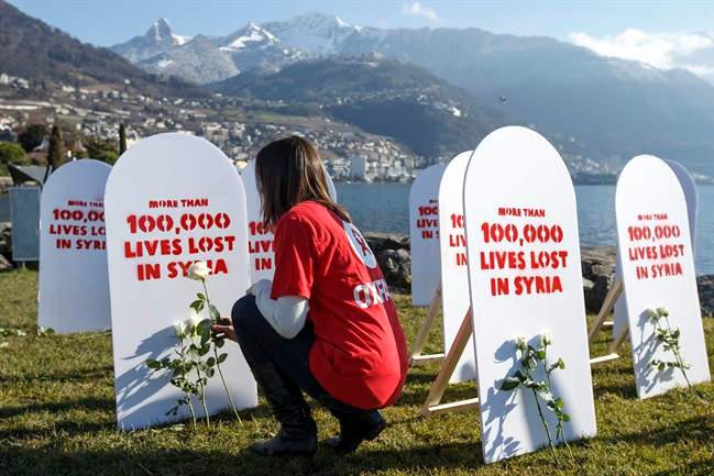 A member of movement Oxford Committee for Famine Relief, "Oxfam", puts a white rose on symbolic gravestones, on the opening day of the Geneva II peace talks on Syria, in Montreux, Switzerland, Wednesday, Jan. 22, 2014.