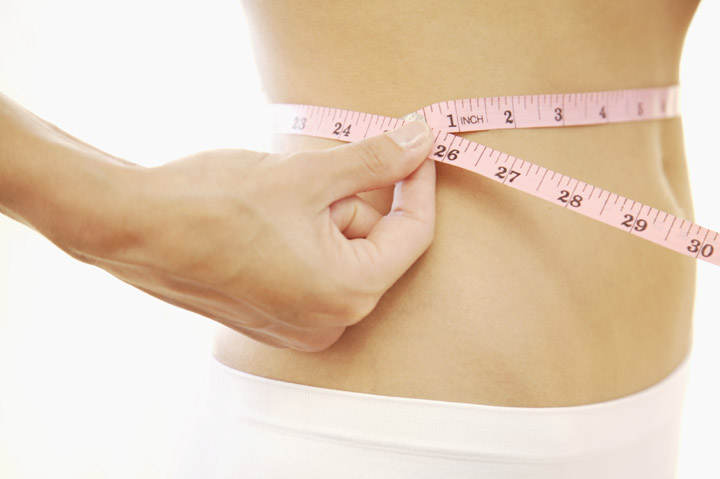 Close up of young woman stomach with measuring tape.