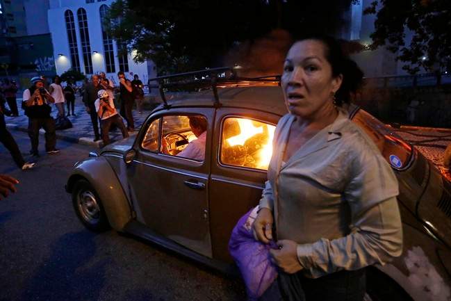  A man drives his car which caught fire when he tried to drive past a burning barricade set up by protesters who were demanding better public services and protesting against the upcoming World Cup soccer tournament in Sao Paulo, Brazil, Saturday, Jan. 25, 2014. 