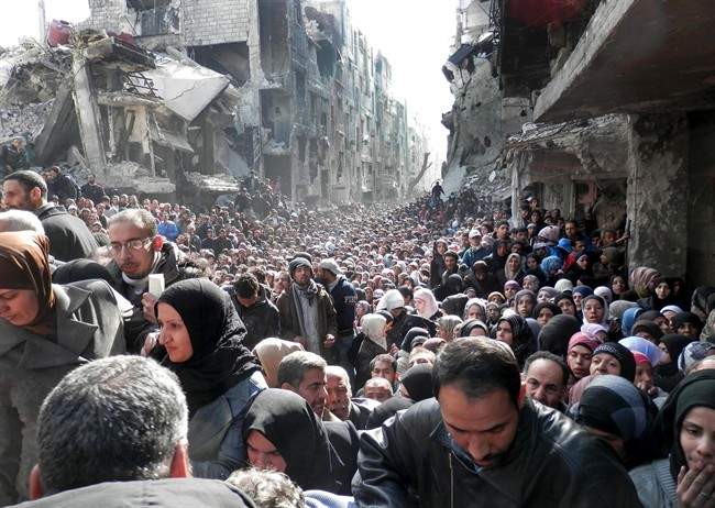This picture taken on Jan. 31, 2014, and released by the United Nations Relief and Works Agency for Palestine Refugees in the Near East (UNRWA), shows residents of the besieged Palestinian camp of Yarmouk, queuing to receive food supplies, in Damascus, Syria. 
